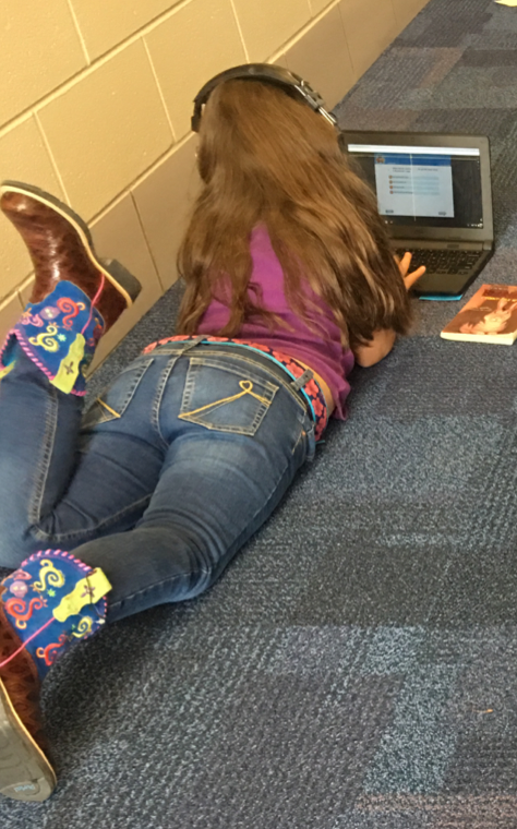 female 3rd grader using a laptop and headphones while laying on the floor