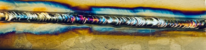 Image of one of Daniel's early TIG welds on stainless steel that is rainbow in color that looks like stacked dimes