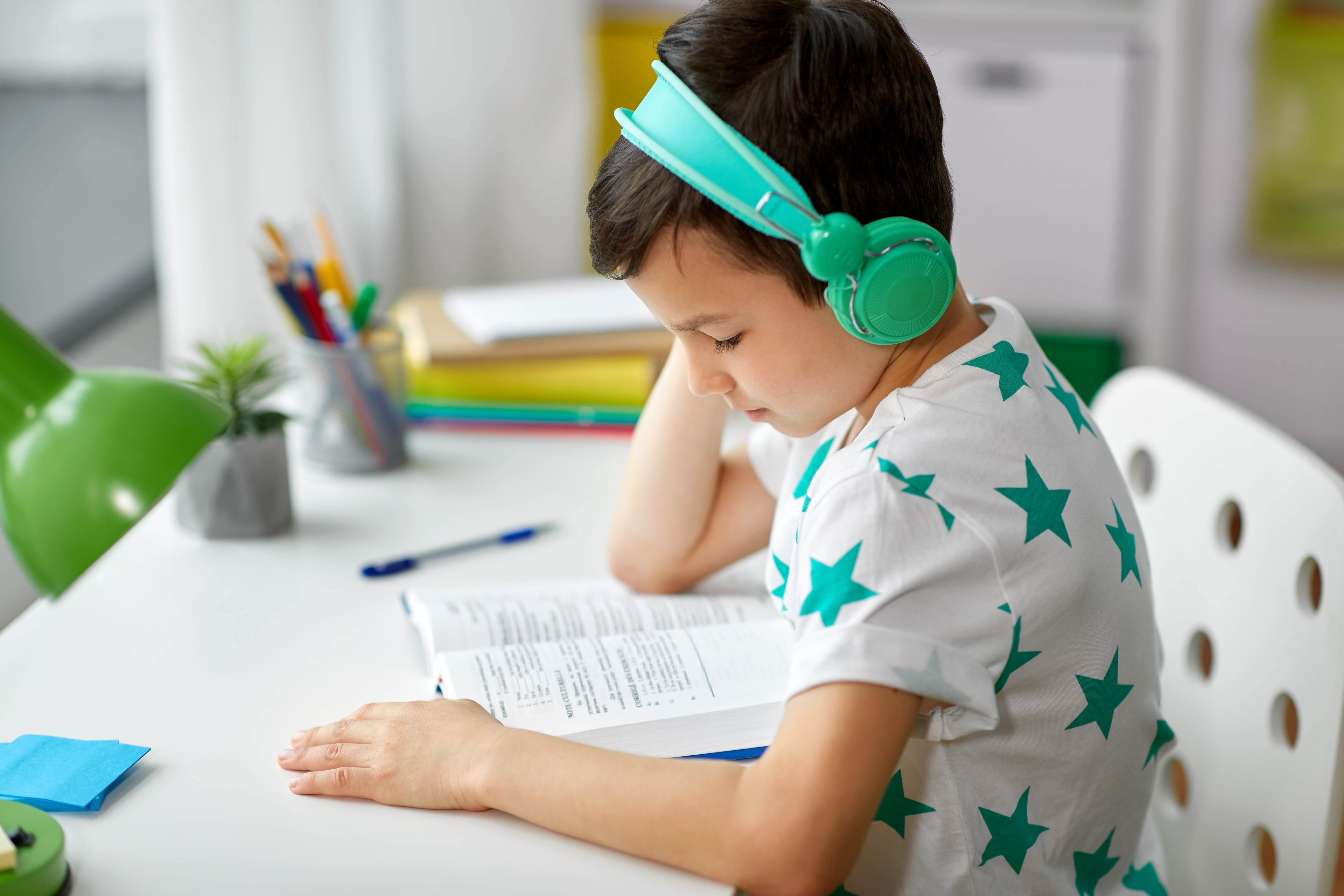 Young student wearing headphones and reading a textbook auditorily