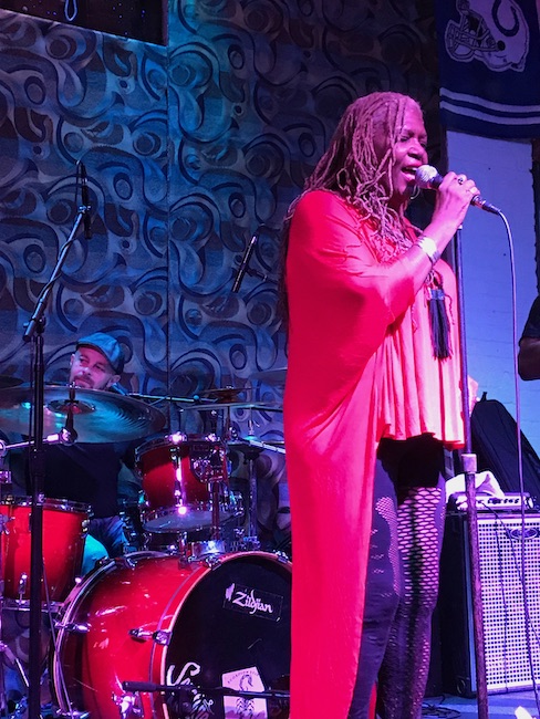 Lead singer of a blues band in a red dress with Daniel sitting on the drumset in the background