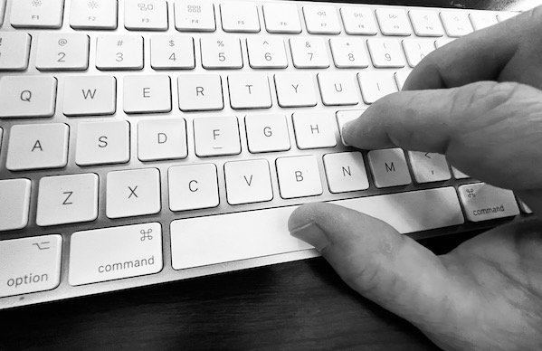 a right hand on the home row of a mac computer keyboard in black and white