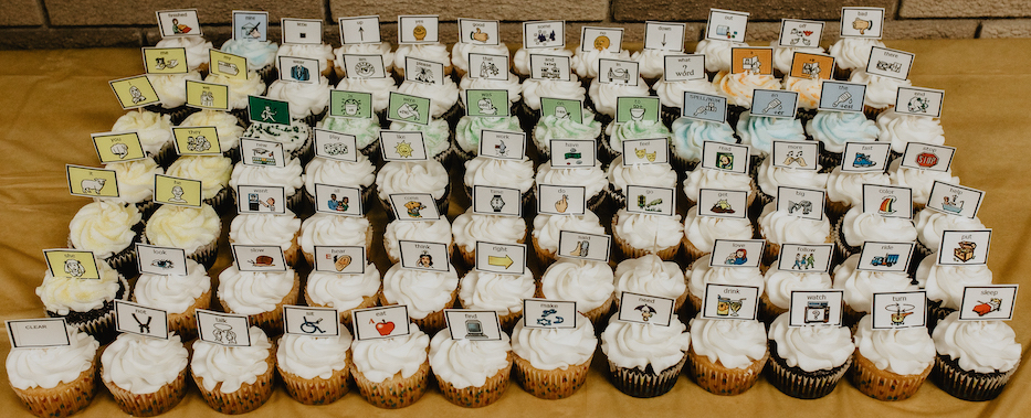 84 cupcakes in a 7 by 12 grid, each with a paper decoration topper representing one of the 84 buttons of the LAMP Words for Life home page.