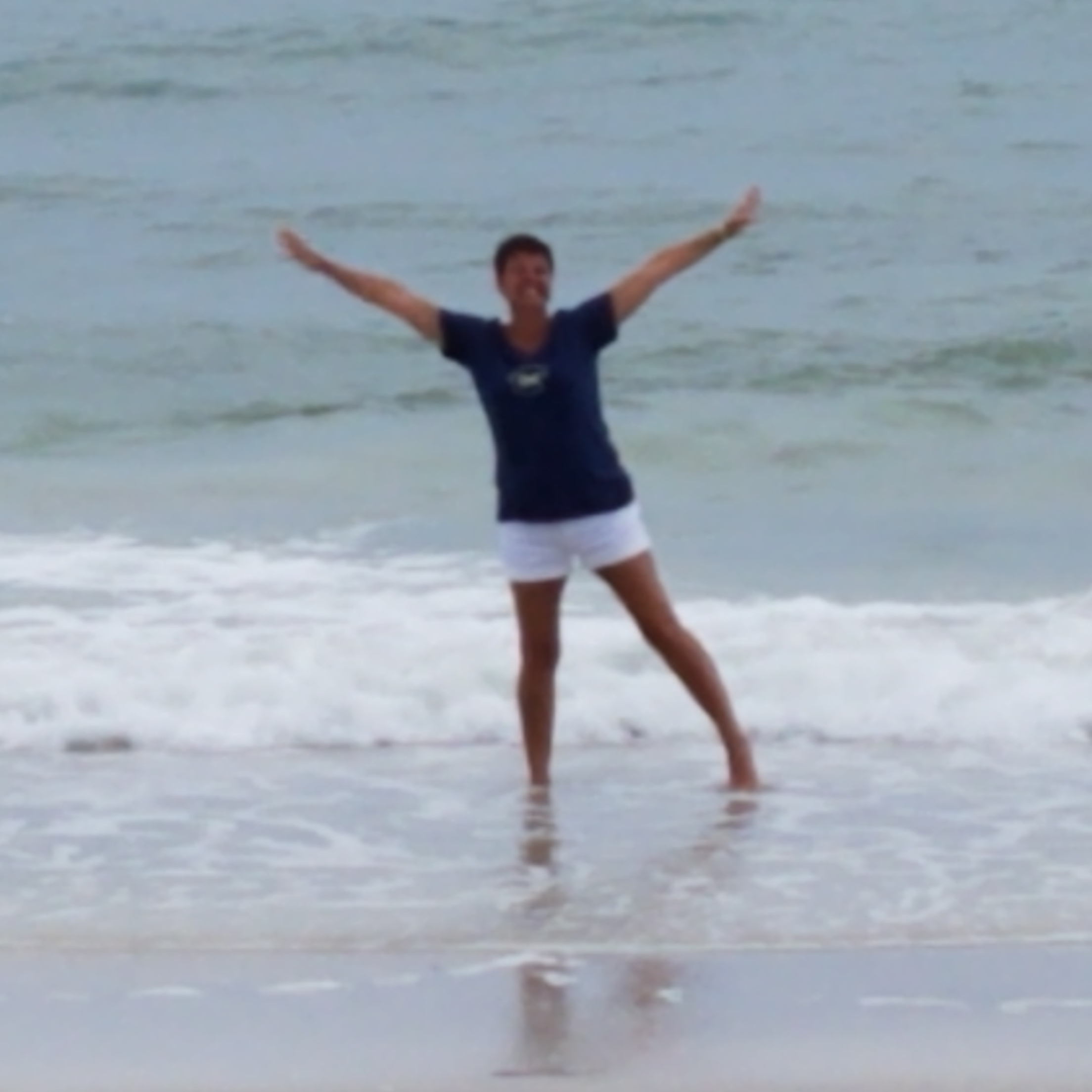 Sandi Smith standing on the beach with arms open like a Y and legs spread apart