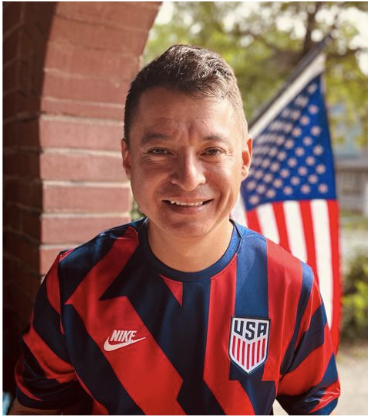 man wearing USA jersey smiling with U.S. flag in background