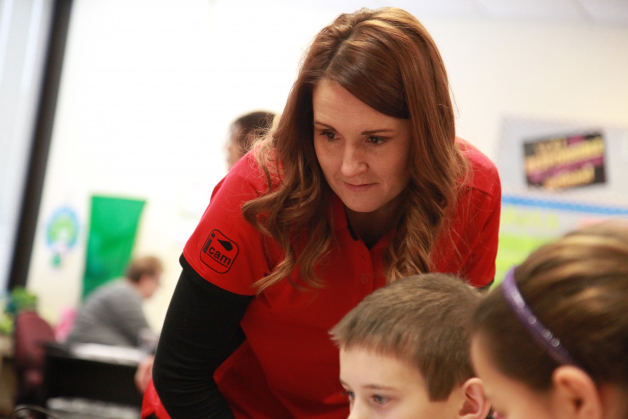 Jena Fahlbush looking down at something with students at their desks